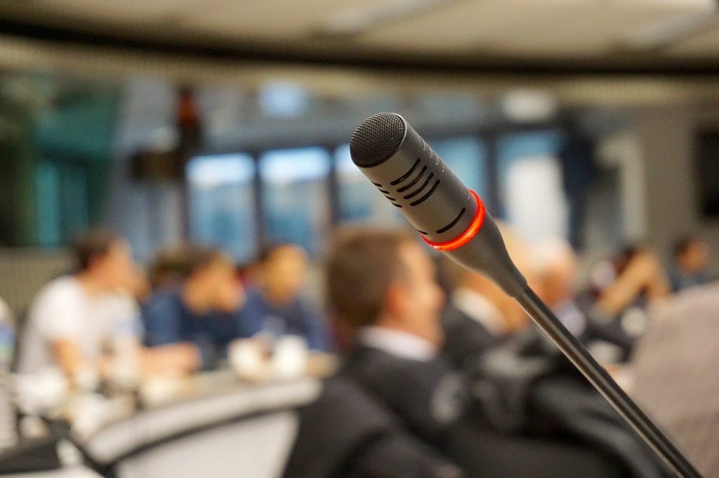 micro de conférence devant une salle pleinde d'auditeurs